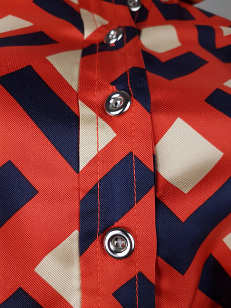 button and closure view: a mannequin displaying a Banana Republic Madmen Collection silk red and navy geometric print shirt shift dress with a 5 button front bodice closure and matching string belt.