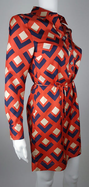 side angle view: a mannequin displaying a Banana Republic Madmen Collection silk red and navy geometric print shirt shift dress with a 5 button front bodice closure and matching string belt.