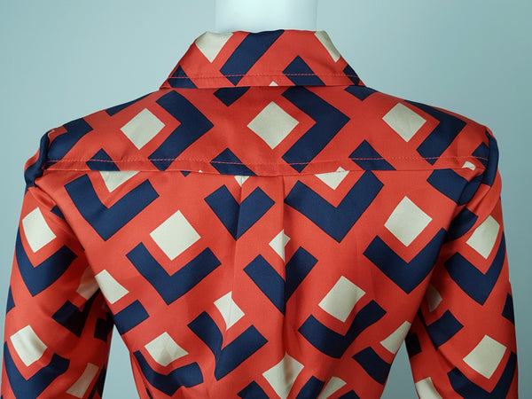 Back shoulder and collar view: a mannequin displaying a Banana Republic Madmen Collection silk red and navy geometric print shirt shift dress with a 5 button front bodice closure and matching string belt.