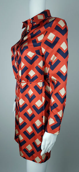 Full side view: a mannequin displaying a Banana Republic Madmen Collection silk red and navy geometric print shirt shift dress with a 5 button front bodice closure and matching string belt.
