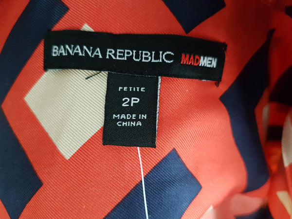 label and tag view: a mannequin displaying a Banana Republic Madmen Collection silk red and navy geometric print shirt shift dress with a 5 button front bodice closure and matching string belt.