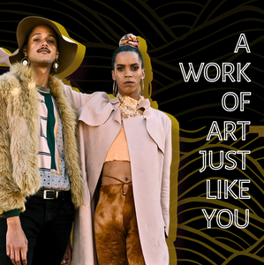 Two stylish individuals stand confidently against a dark patterned backdrop. One wears a tan fur jacket, geometric print blouse, and wide-brimmed hat; the other wears a pale pink coat over a lace top and high-waisted brown pants. The text beside them reads “A work of art just like you."