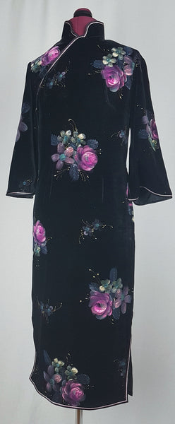 Front view of a 1950s black velvet cheongsam qipao dress with a mandarin collar, contrasting piping and hand-painted pink floral design displayed on a mannequin 