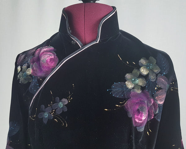 Front collar and shoulder view of a 1950s black velvet cheongsam qipao dress with a mandarin collar, contrasting piping and hand-painted pink floral design displayed on a mannequin 