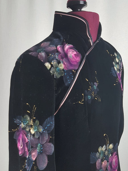 collar and shoulder three quarter view of a 1950s black velvet cheongsam qipao dress with a mandarin collar, contrasting piping and hand-painted pink floral design displayed on a mannequin 