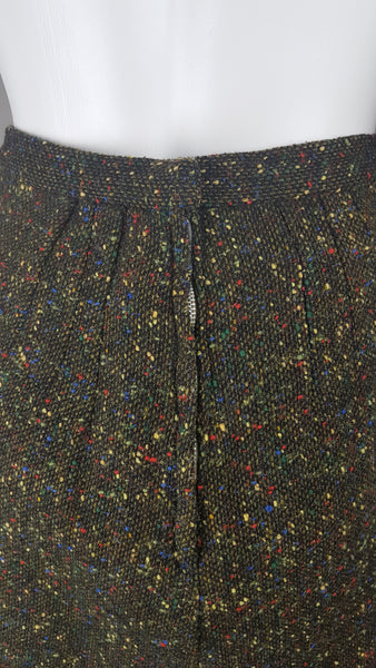 zip and hook and eye closure of a vintage 1960s dark green bouclé A-line skirt with colorful confetti flecks in red, yellow, blue, and green, shown on a mannequin against a neutral background.