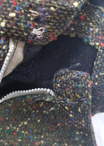 Zip and hook and eye closure of a vintage 1960s dark green bouclé A-line skirt with colorful confetti flecks in red, yellow, blue, and green, shown on a mannequin against a neutral background.