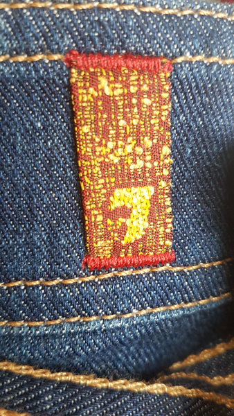 Close-up of the red-and-gold 7 For All Mankind label attached to the rear welt pocket of on 7 For All Mankind indigo jeans