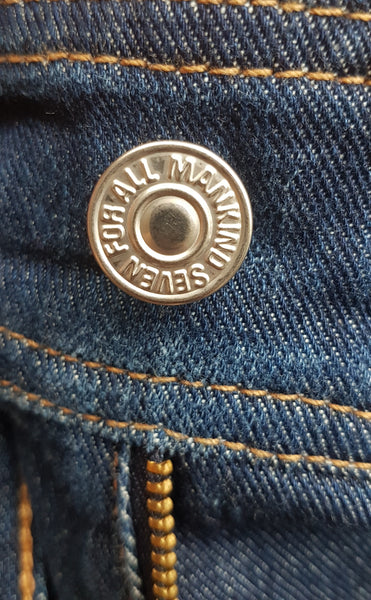 Close-up of the branded silver waistband button and gold-tone YKK zip fly on 7 For All Mankind indigo jeans