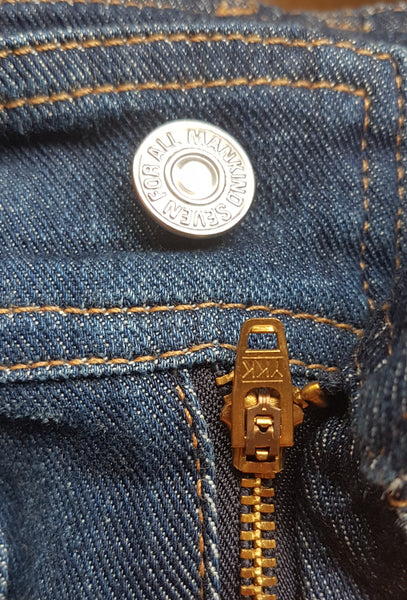 Close-up of the branded silver waistband button and gold-tone YKK zip fly on 7 For All Mankind indigo jeans