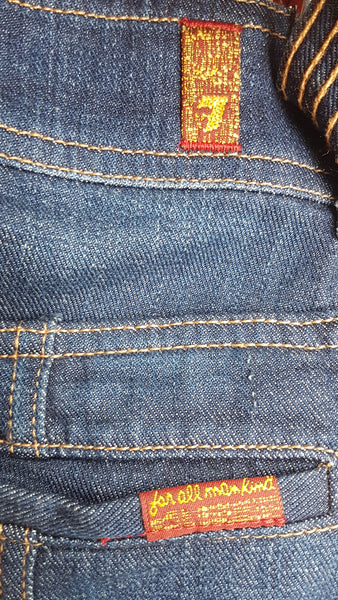 Close-up of the red-and-gold 7 For All Mankind label attached to the rear welt pocket of on 7 For All Mankind indigo jeans