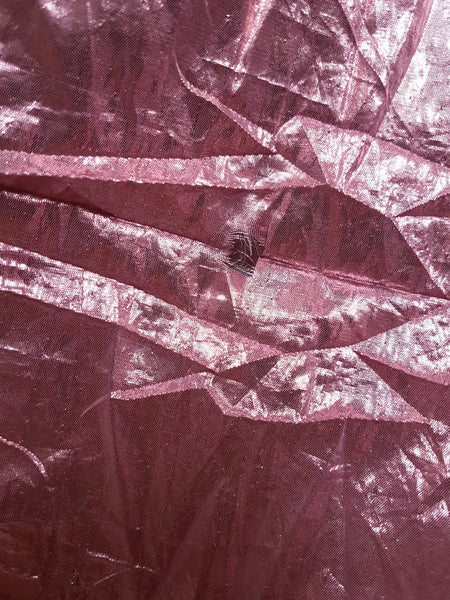 Close-up of crinkled metallic pink lamé fabric showing surface abrasions and wear