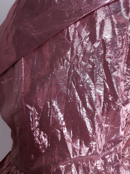 Close-up of crinkled metallic pink lamé fabric showing surface abrasions and wear
