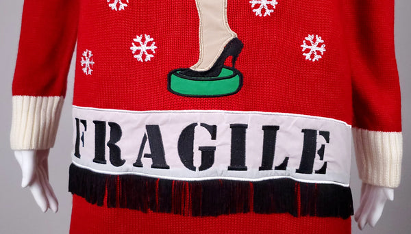 Close-up of the white FRAGILE appliqué band and black fringe across the lower front
