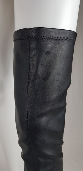 Black vegan leather over-the-knee boots with a smooth texture and a slight sheen, featuring a partial side zip closure and an almond-shaped toe displayed on a mannequin - thigh front view