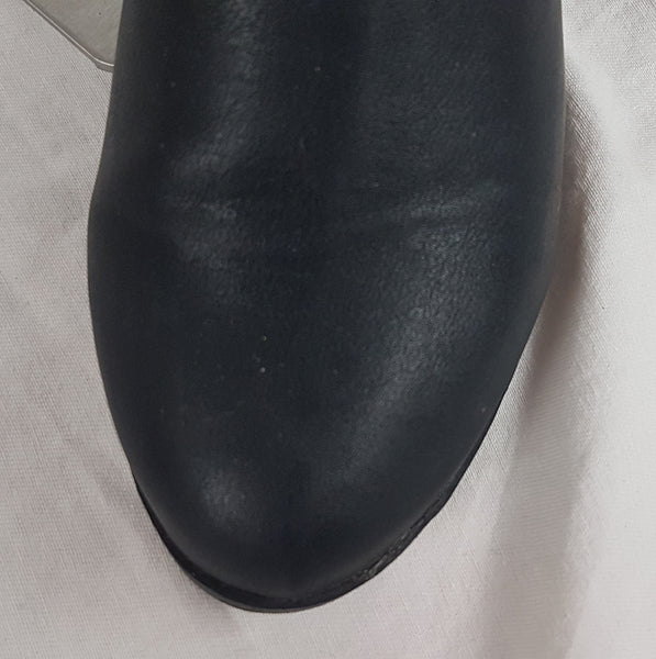 Black vegan leather over-the-knee boots with a smooth texture and a slight sheen, featuring a partial side zip closure - almond-shaped toe view  