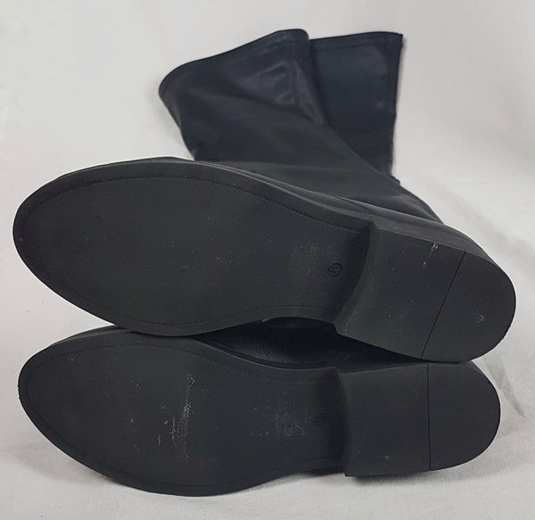 Black vegan leather over-the-knee boots with a smooth texture and a slight sheen, featuring a partial side zip closure and an almond-shaped toe - flatlay, bottom soles view