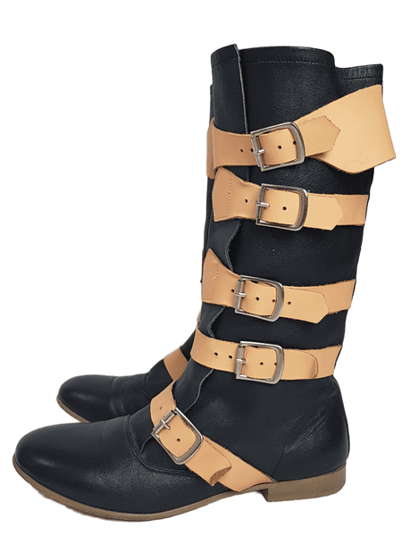 Side view of a pair of black mid-calf leather boots wrapped with contrasting tan straps and antiqued metal buckles