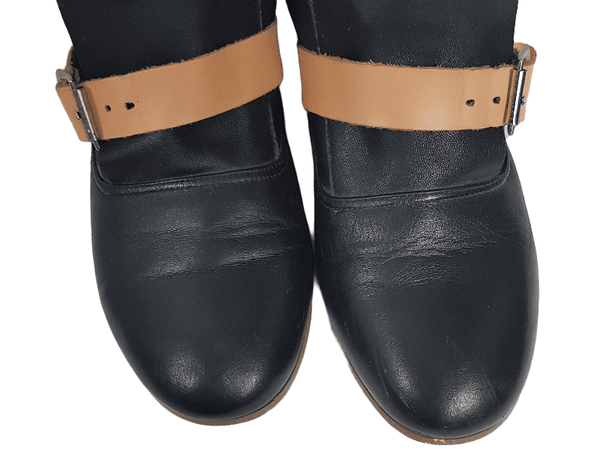 Round toe view of a pair of black mid-calf leather boots wrapped with contrasting tan straps 