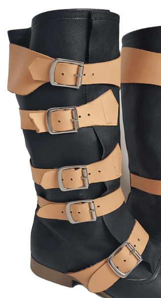 Close up Three quarter view of a pair of black mid-calf leather boots wrapped with contrasting tan straps and antiqued metal buckles
