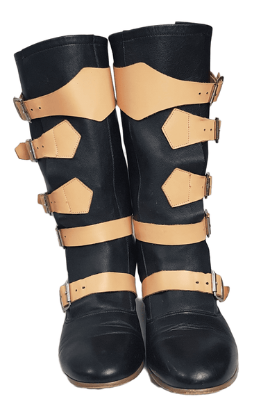Front view of a pair of black mid-calf leather boots wrapped with contrasting tan straps and antiqued metal buckles