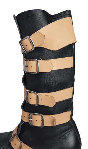 Side view of a pair of black mid-calf leather boots wrapped with contrasting tan straps and antiqued metal buckles