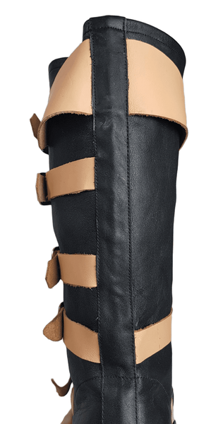 Back view of a pair of black mid-calf leather boots wrapped with contrasting tan straps and antiqued metal buckles