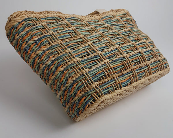 Tote bag resting on its side showing the broad base and multicoloured woven exterior