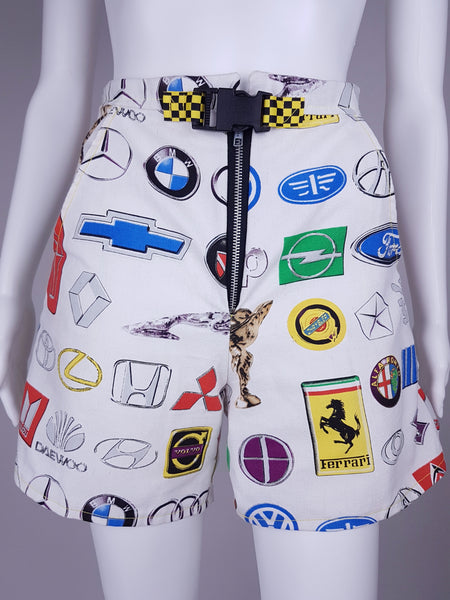 Front view of high-waisted automotive-print shorts with an exposed metal zipper and checkerboard buckle belt