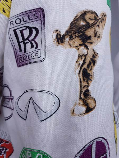 Fabric close-up showing illustrated Rolls-Royce emblems, a hood ornament and the textured white weave