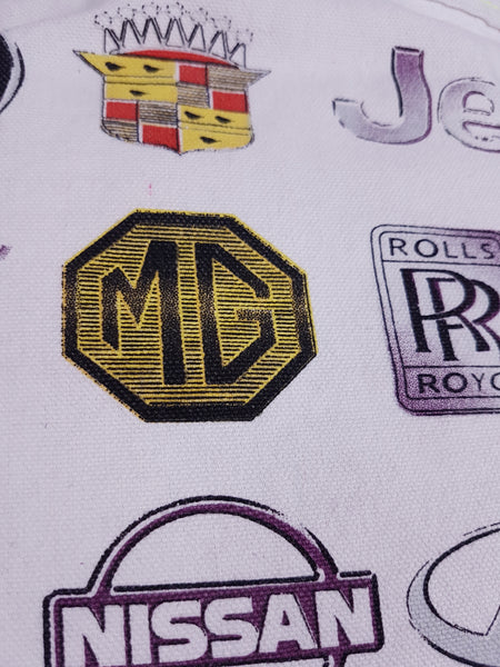 Fabric close-up showing MG, Rolls-Royce, Nissan and Cadillac emblems on the textured white weave