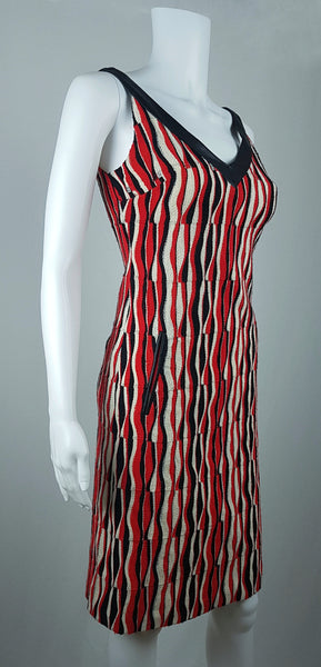 Three-quarter front view of a modern Tocca red, black and ivory Op Art woven sheath dress with black V-neck trim displayed on a mannequin