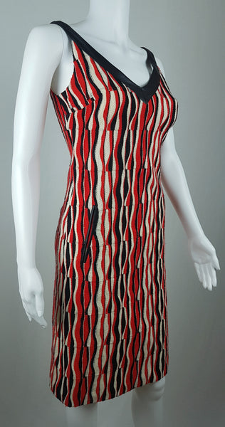 Three-quarter front view of a modern Tocca red, black and ivory Op Art woven sheath dress with black V-neck trim displayed on a mannequin