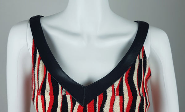 Close-up of the broad black leather-look V-neck trim on a modern Tocca red, black and ivory Op Art woven sheath dress with black V-neck trim displayed on a mannequin