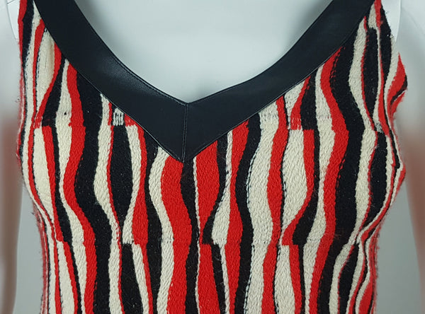 Close-up of the broad black leather-look V-neck trim on a modern Tocca red, black and ivory Op Art woven sheath dress with black V-neck trim displayed on a mannequin