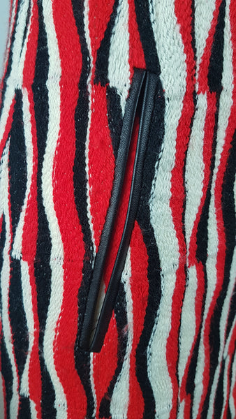 Close-up of the black leather-look faux pocket accent on a modern Tocca red, black and ivory Op Art woven sheath dress with black V-neck trim displayed on a mannequin