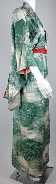 Three-quarter side view of a vintage green floral silk kimono styled with a contrasting red scarf at the waist.