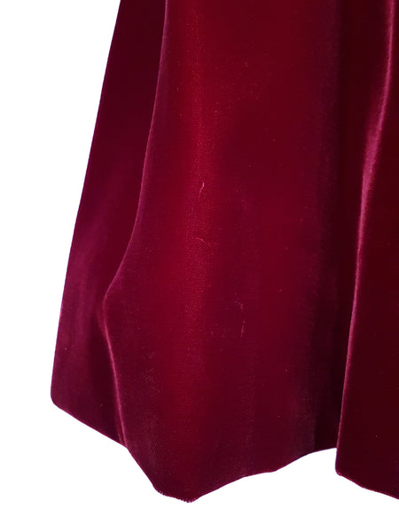 Skirt and hem view of a circa mid-1950s Suzy Perette dark red velvet dress with square neckline, narrow straps and full skirt displayed on a mannequin 