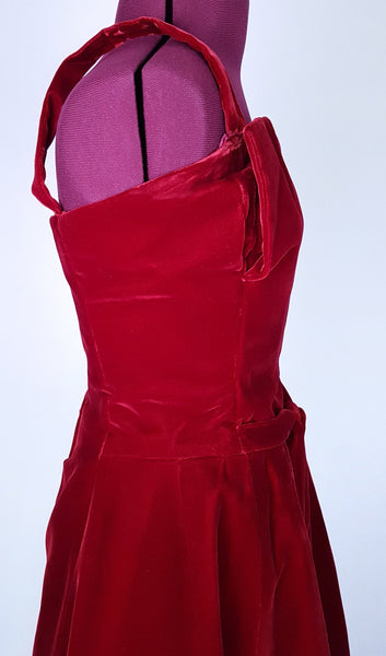 Side bodice view of a circa mid-1950s Suzy Perette dark red velvet dress with square neckline, narrow straps and full skirt displayed on a mannequin 