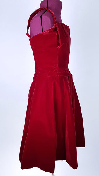 Three-quarter side view of a circa mid-1950s Suzy Perette dark red velvet dress with square neckline, narrow straps and full skirt displayed on a mannequin 