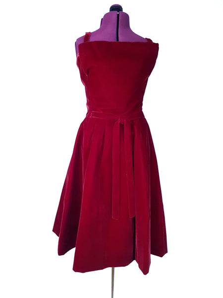 Front view of a circa mid-1950s Suzy Perette dark red velvet dress with fitted bodice, pleated skirt and velvet waist ties displayed on a mannequin 