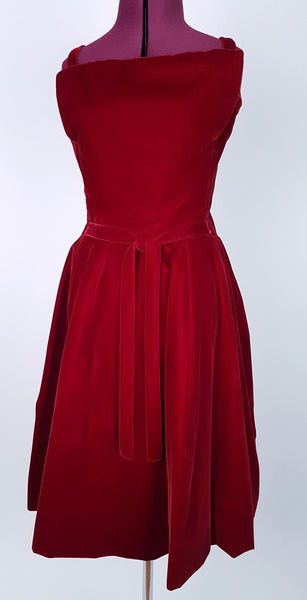 Front view of a circa mid-1950s Suzy Perette dark red velvet dress with fitted bodice, pleated skirt and velvet waist ties displayed on a mannequin 