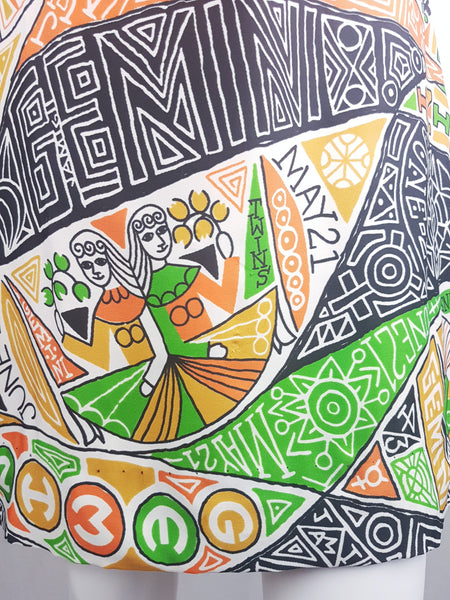 Close-up of the orange, green, mustard, black and white Gemini twins novelty print on a late 1960s zodiac dress.