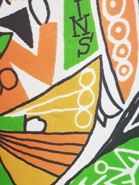 Close-up of the minor flaws on an orange, green, mustard, black and white novelty print on a late 1960s zodiac dress.