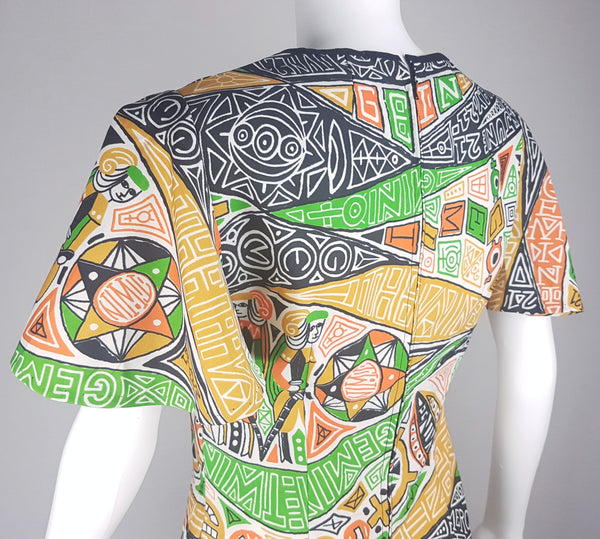 Close-up back shoulder three quarter view of a 1960s Gemini zodiac print dress, showing the scoop neckline and flared butterfly sleeve, displayed on a mannequin