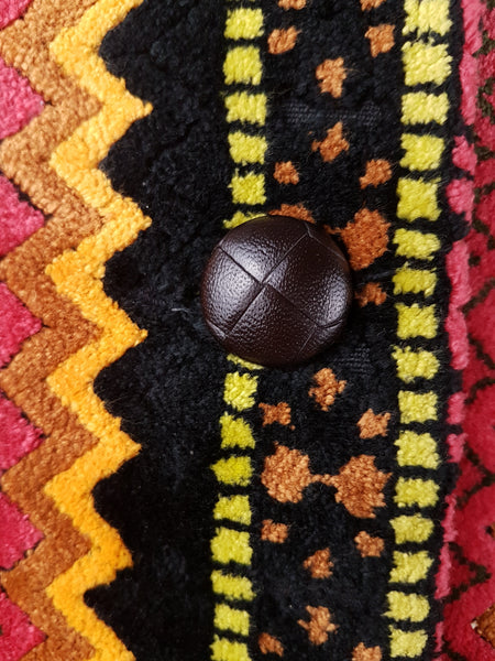 Close-up of a dark brown molded basketweave-effect button on the colourful geometric chenille fabric of a vintage 1960s Trego’s Westwear coat