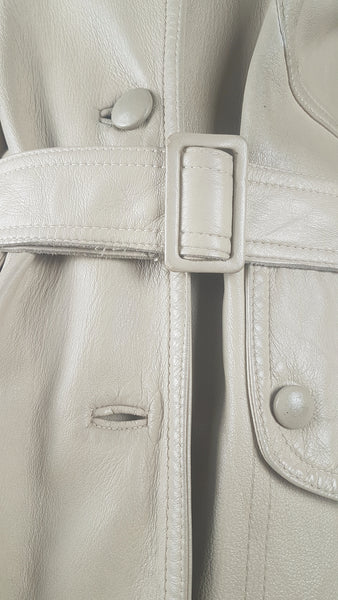 Closeup belt and buttons view on a vintage 1970s sand-coloured leather trench coat with tonal buttons, shoulder tabs and a matching belt displayed on a mannequin