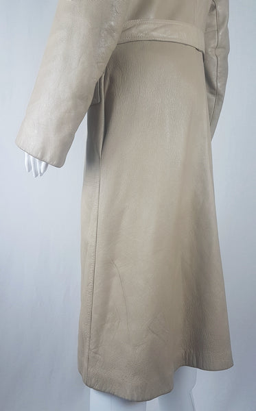 Back sleeves and bottom hem view of a vintage 1970s sand-coloured leather trench coat with tonal buttons, shoulder tabs and a matching belt displayed on a mannequin