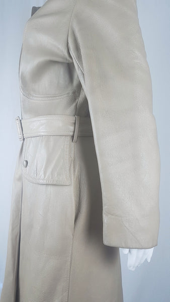 Closeup side sleeve view on a vintage 1970s sand-coloured leather trench coat with tonal buttons, shoulder tabs and a matching belt displayed on a mannequin
