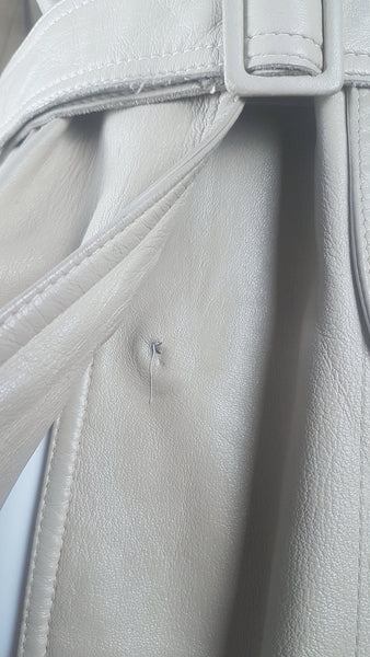Closeup to show missing button on a vintage 1970s sand-coloured leather trench coat with tonal buttons, shoulder tabs and a matching belt displayed on a mannequin